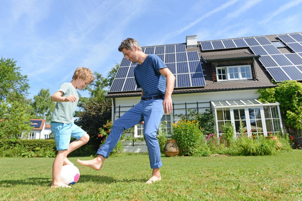 family playing soccer in front of house with solar panels